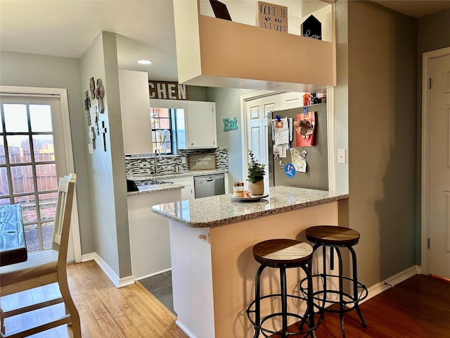 kitchen featuring white cabinetry, light stone counters, stainless steel dishwasher, and kitchen peninsula