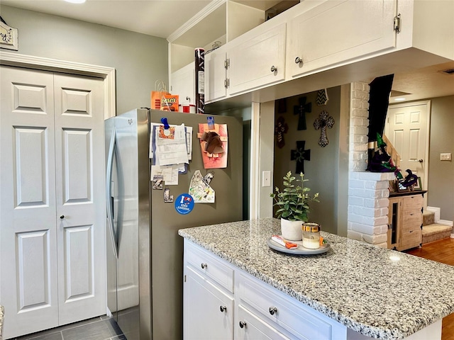 kitchen featuring light stone counters, kitchen peninsula, stainless steel refrigerator, and white cabinets