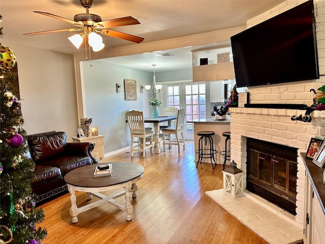 living room featuring a brick fireplace, ceiling fan, and light hardwood / wood-style flooring