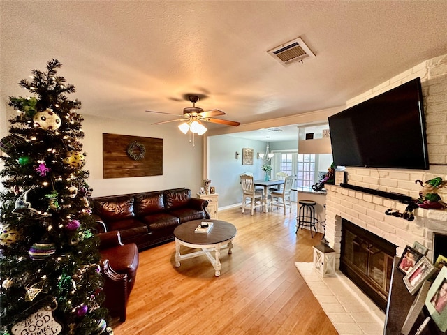 living room featuring ceiling fan, a fireplace, a textured ceiling, and light wood-type flooring