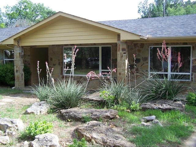 exterior space with stone siding and roof with shingles