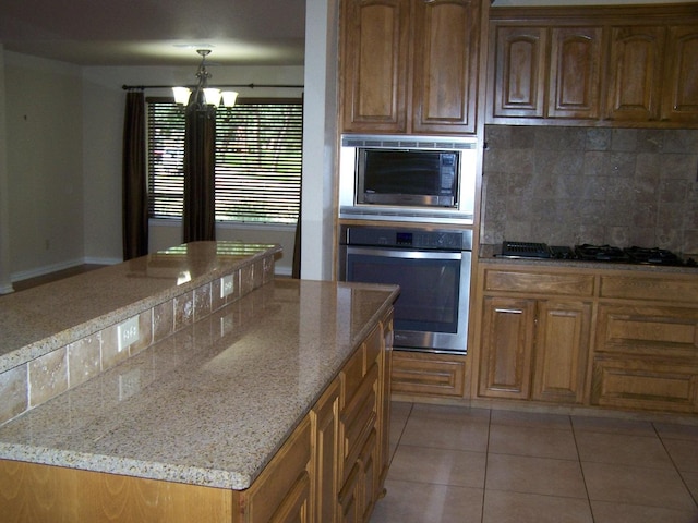 kitchen featuring backsplash, light tile patterned flooring, stainless steel oven, built in microwave, and light stone countertops