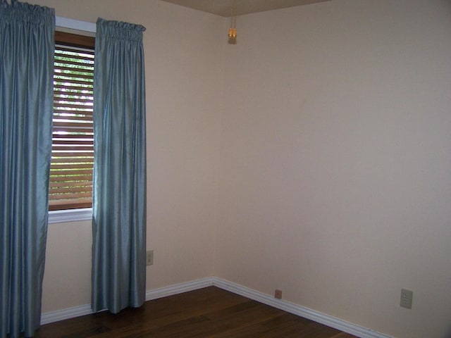 spare room with baseboards and dark wood-style flooring