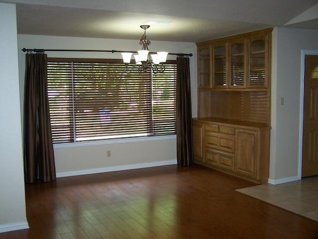 unfurnished dining area featuring baseboards, a notable chandelier, and wood finished floors