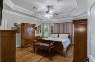 bedroom with wood-type flooring, ornamental molding, and a tray ceiling