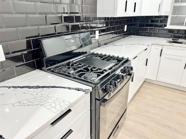 kitchen featuring white cabinets, light stone countertops, stainless steel gas range, and light hardwood / wood-style floors