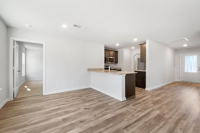 kitchen with sink, appliances with stainless steel finishes, light stone counters, kitchen peninsula, and light wood-type flooring