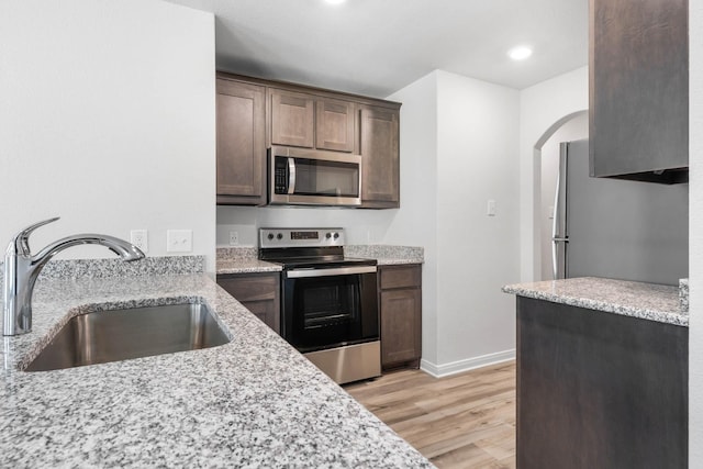 kitchen featuring light stone counters, stainless steel appliances, light hardwood / wood-style floors, and sink