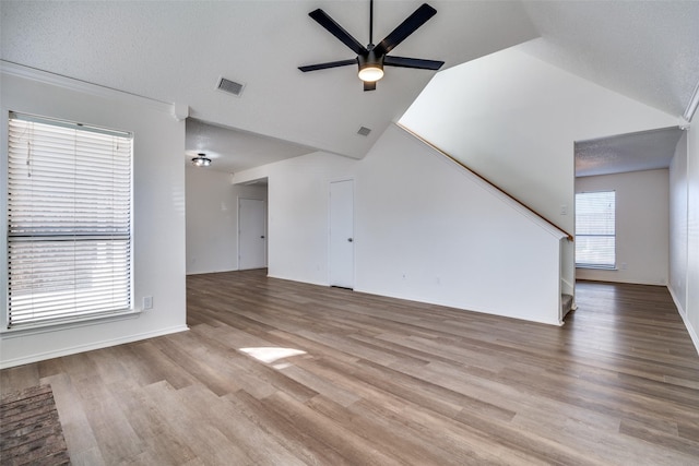 unfurnished living room with ceiling fan, lofted ceiling, a textured ceiling, and light wood-type flooring