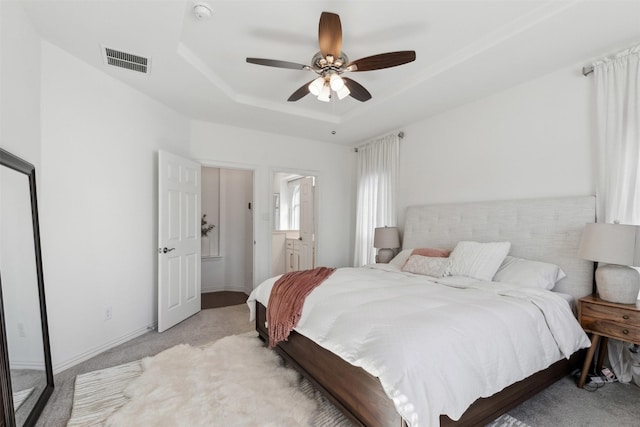 carpeted bedroom featuring ceiling fan, a raised ceiling, and ensuite bath