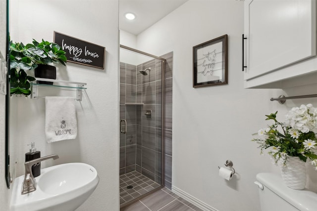 bathroom featuring a shower with door, sink, and toilet