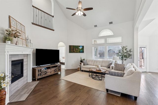 living room featuring dark wood-type flooring, ceiling fan, and a tiled fireplace