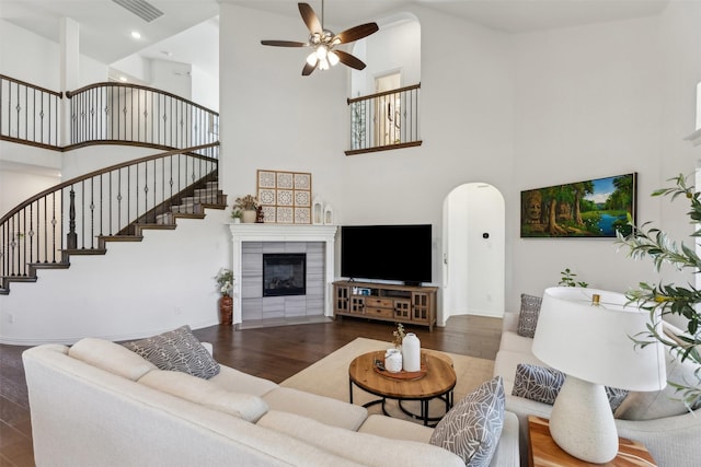 living room featuring ceiling fan, dark hardwood / wood-style floors, a tile fireplace, and a towering ceiling