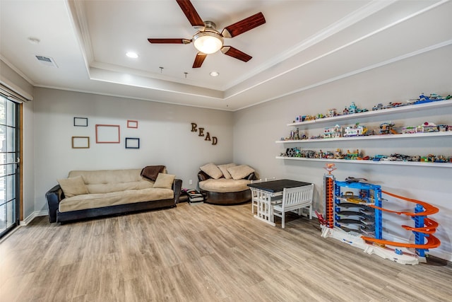 living room featuring a tray ceiling, ornamental molding, ceiling fan, and light wood-type flooring