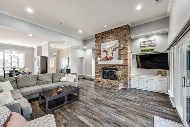 living room with crown molding, dark wood-type flooring, a chandelier, and a fireplace