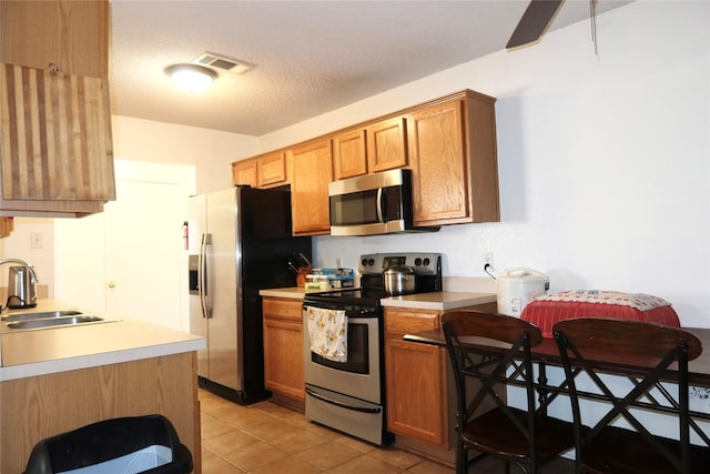 kitchen featuring sink, light tile patterned flooring, a textured ceiling, and appliances with stainless steel finishes