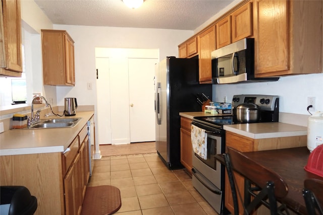 kitchen with appliances with stainless steel finishes, sink, light tile patterned floors, and a textured ceiling