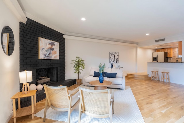 living room with ornamental molding, a brick fireplace, and light wood-type flooring