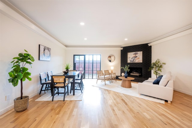 dining area with ornamental molding, a brick fireplace, and light hardwood / wood-style flooring