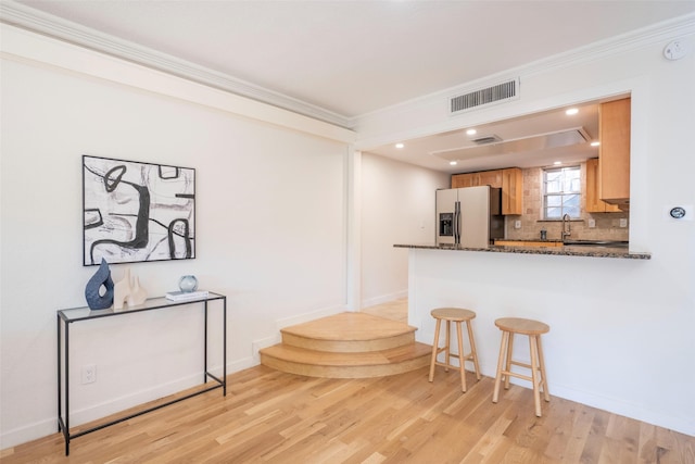 kitchen with decorative backsplash, dark stone counters, ornamental molding, light hardwood / wood-style floors, and stainless steel fridge with ice dispenser