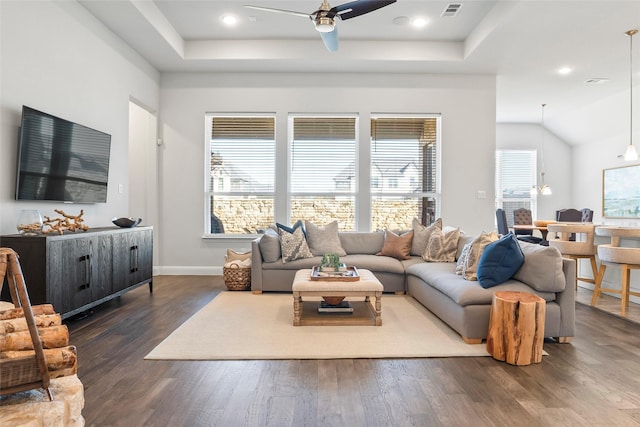 living room with a raised ceiling, dark wood-type flooring, and ceiling fan