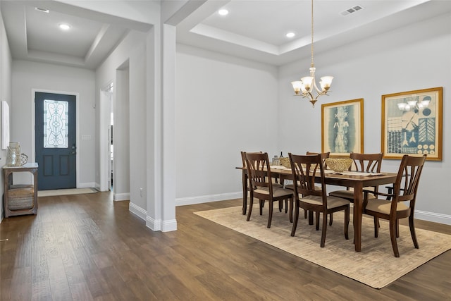 dining area featuring a raised ceiling, dark wood-type flooring, and an inviting chandelier