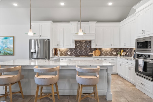 kitchen with appliances with stainless steel finishes, decorative light fixtures, and a center island with sink