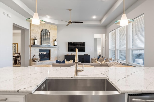 kitchen featuring a tray ceiling, light stone counters, decorative light fixtures, and a stone fireplace