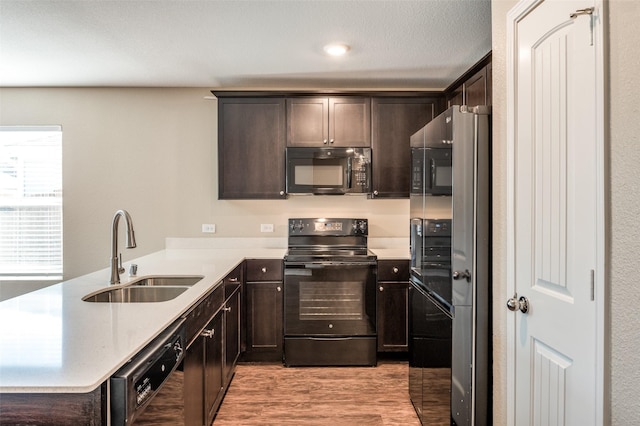 kitchen featuring light wood-type flooring, dark brown cabinetry, sink, and black appliances