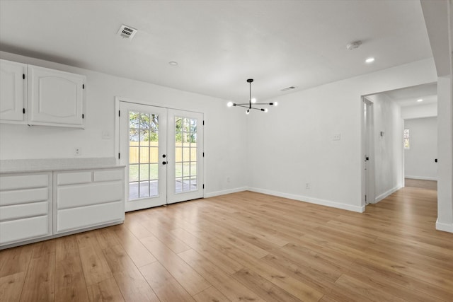 unfurnished dining area featuring an inviting chandelier, light hardwood / wood-style flooring, and french doors