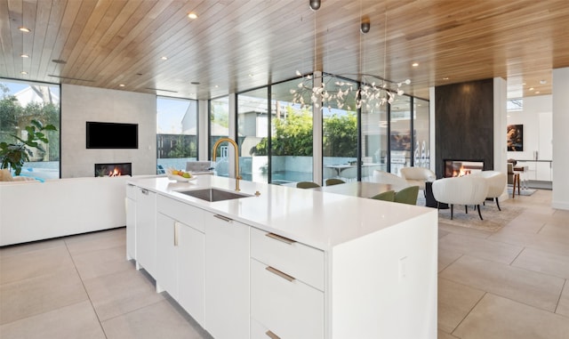 kitchen with a kitchen island with sink, sink, white cabinets, and a multi sided fireplace