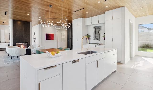 kitchen featuring sink, white cabinets, light tile patterned floors, a center island with sink, and wooden ceiling