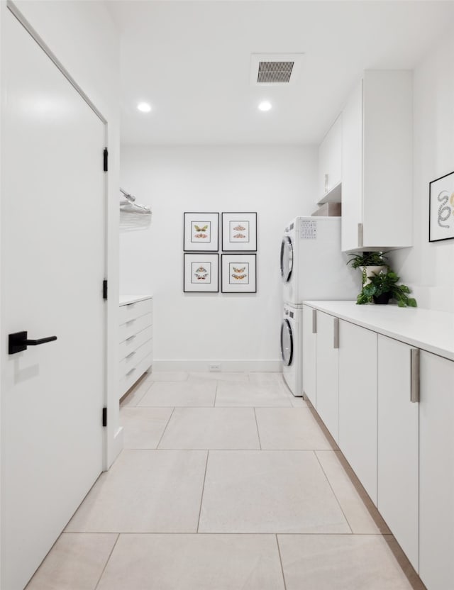 laundry area featuring stacked washer and dryer, light tile patterned floors, and cabinets