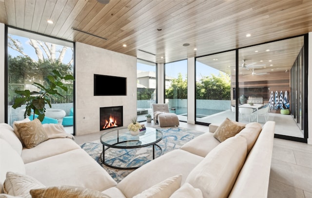 sunroom / solarium featuring wood ceiling, plenty of natural light, a large fireplace, and ceiling fan