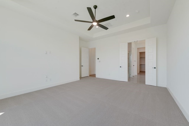 unfurnished bedroom with light carpet, a tray ceiling, and ceiling fan