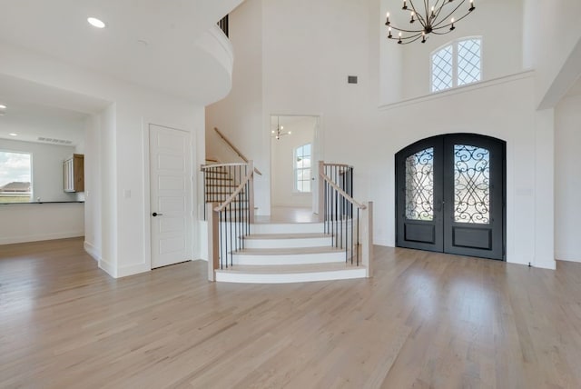 foyer entrance with a notable chandelier, french doors, a healthy amount of sunlight, and light wood-type flooring