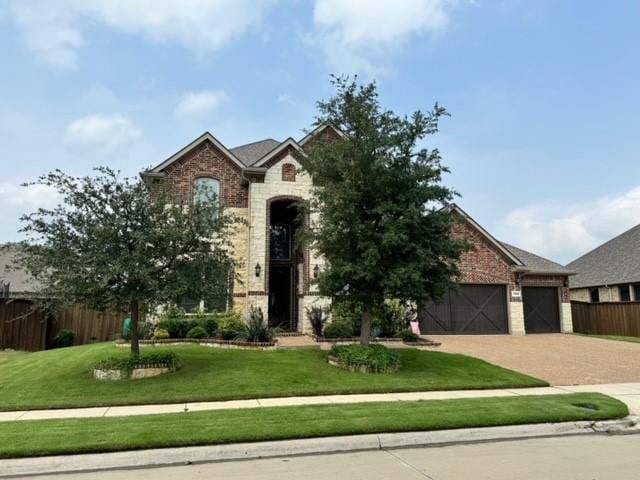 french country home featuring decorative driveway, brick siding, an attached garage, a front yard, and fence