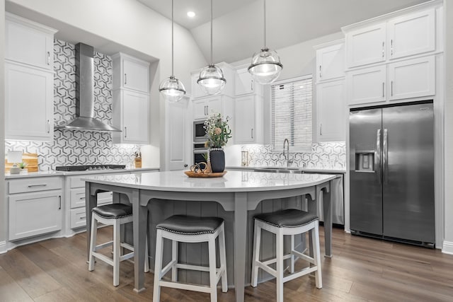 kitchen with appliances with stainless steel finishes, decorative light fixtures, white cabinetry, a center island, and wall chimney exhaust hood