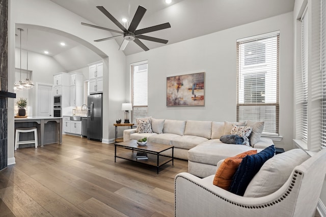 living room with high vaulted ceiling, ceiling fan, and light hardwood / wood-style flooring