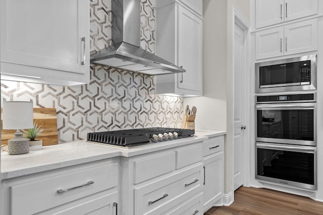 kitchen featuring white cabinetry, wall chimney range hood, tasteful backsplash, and stainless steel appliances