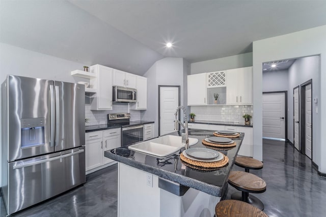 kitchen featuring vaulted ceiling, appliances with stainless steel finishes, white cabinetry, sink, and a kitchen island with sink