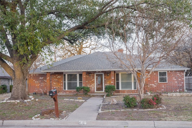 ranch-style home with brick siding, roof with shingles, and a chimney