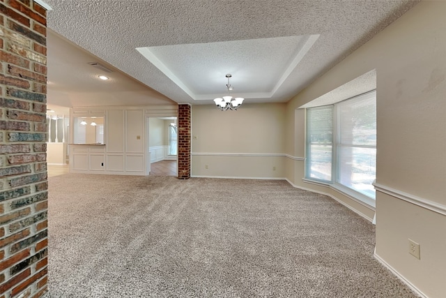 unfurnished room featuring a notable chandelier, a textured ceiling, baseboards, carpet flooring, and a raised ceiling