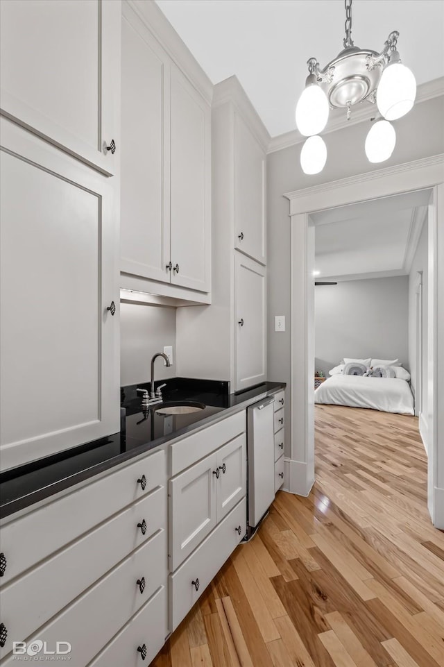 kitchen featuring white cabinetry, crown molding, decorative light fixtures, and sink