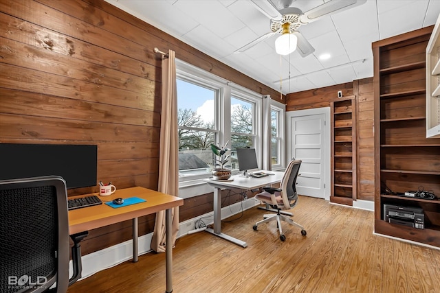 office area featuring ceiling fan, built in shelves, light hardwood / wood-style floors, and wood walls