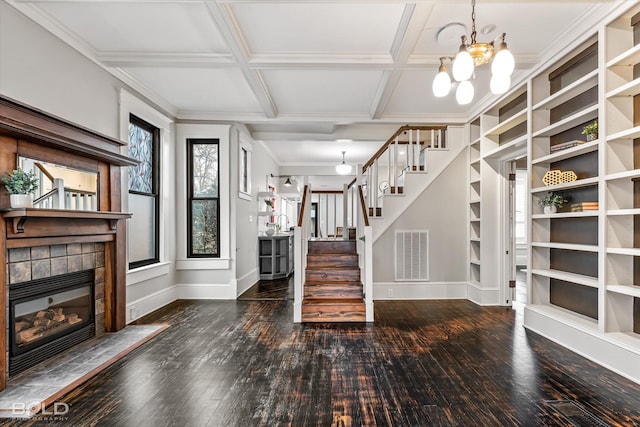 entrance foyer with coffered ceiling, ornamental molding, dark hardwood / wood-style flooring, a notable chandelier, and a tiled fireplace