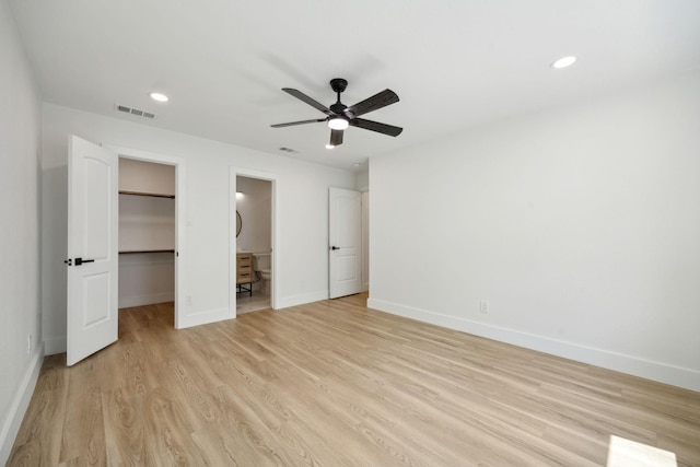 unfurnished bedroom featuring connected bathroom, a spacious closet, ceiling fan, light wood-type flooring, and a closet