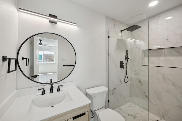 bathroom with ceiling fan, tiled shower, vanity, and toilet