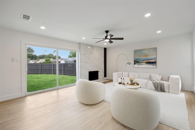 living room featuring a premium fireplace, ceiling fan, and light wood-type flooring