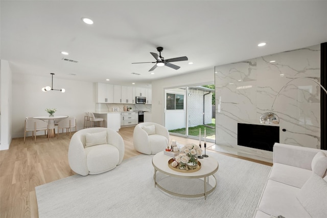 living room with a premium fireplace, ceiling fan, and light wood-type flooring